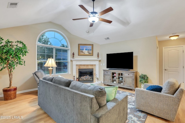 living room with a tiled fireplace, light hardwood / wood-style flooring, ceiling fan, and vaulted ceiling