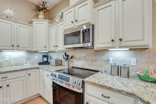 kitchen with tasteful backsplash, appliances with stainless steel finishes, light wood-type flooring, and light stone counters