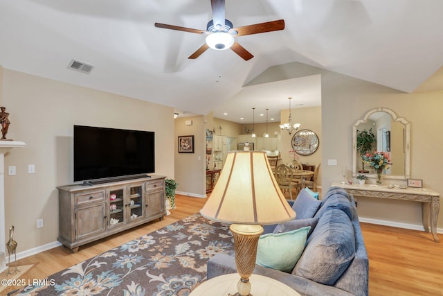 living room featuring ceiling fan with notable chandelier, vaulted ceiling, and light wood-type flooring