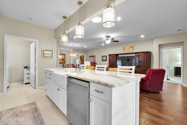 kitchen featuring white cabinets, light stone counters, open floor plan, a kitchen island with sink, and stainless steel dishwasher