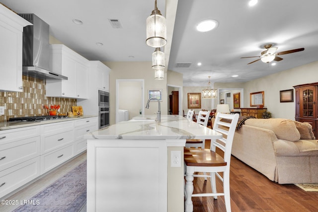 kitchen featuring visible vents, wall chimney exhaust hood, a breakfast bar, open floor plan, and stainless steel appliances