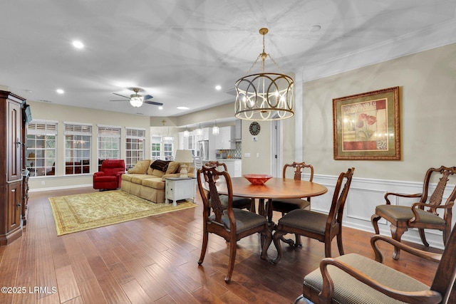 dining area featuring ceiling fan with notable chandelier, wainscoting, dark wood finished floors, and recessed lighting