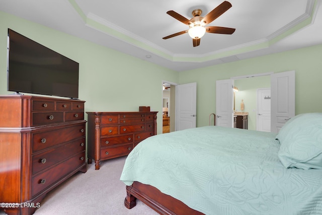 bedroom featuring crown molding, a raised ceiling, light colored carpet, ensuite bathroom, and a ceiling fan