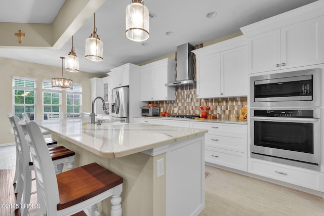 kitchen featuring stainless steel appliances, tasteful backsplash, white cabinets, a sink, and wall chimney exhaust hood