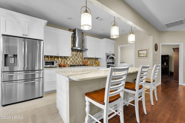 kitchen with wall chimney exhaust hood, visible vents, stainless steel appliances, and backsplash