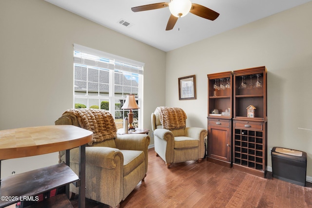 sitting room with a ceiling fan, visible vents, and dark wood finished floors