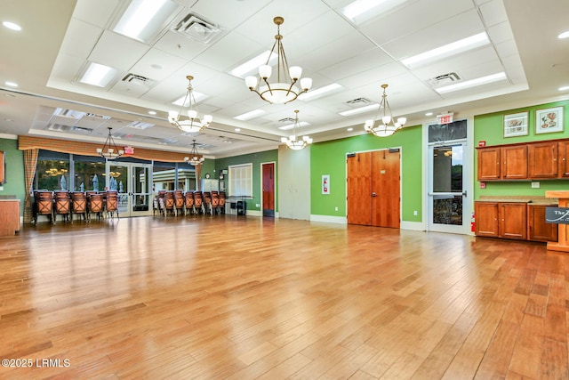 interior space featuring light wood-type flooring, a raised ceiling, visible vents, and a notable chandelier