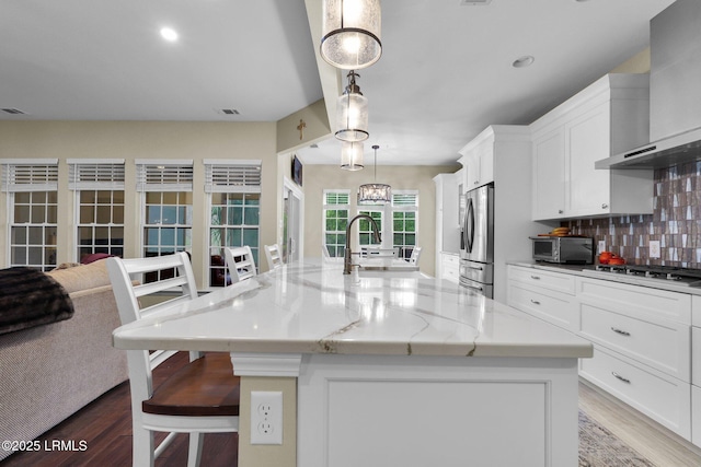 kitchen featuring stainless steel refrigerator with ice dispenser, a breakfast bar area, tasteful backsplash, wall chimney range hood, and gas cooktop