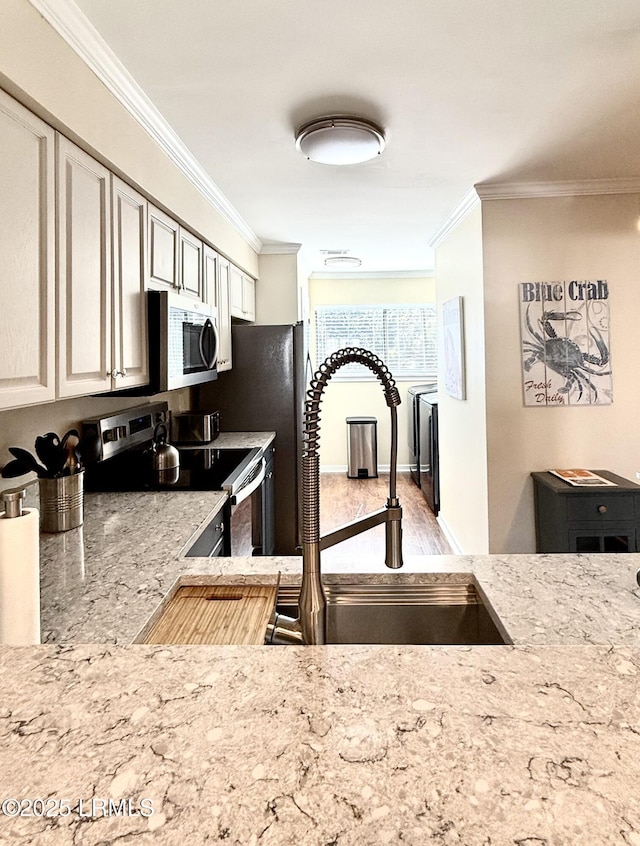 kitchen with appliances with stainless steel finishes, wood-type flooring, sink, light stone counters, and ornamental molding