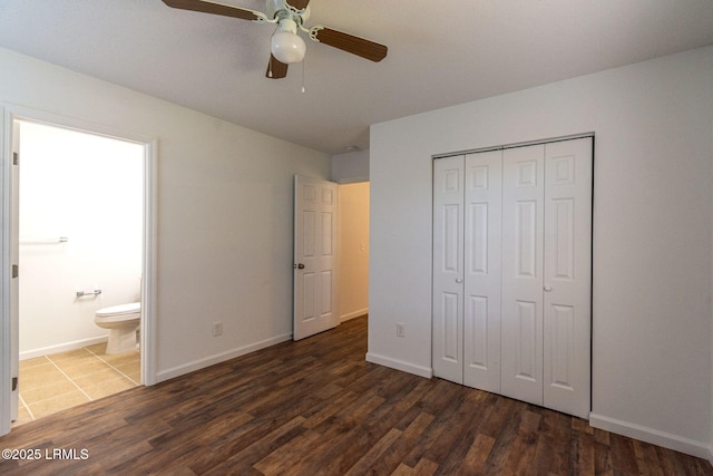 unfurnished bedroom featuring baseboards, a ceiling fan, ensuite bath, dark wood-type flooring, and a closet