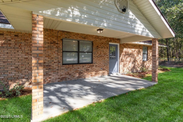 doorway to property with brick siding, a lawn, and fence