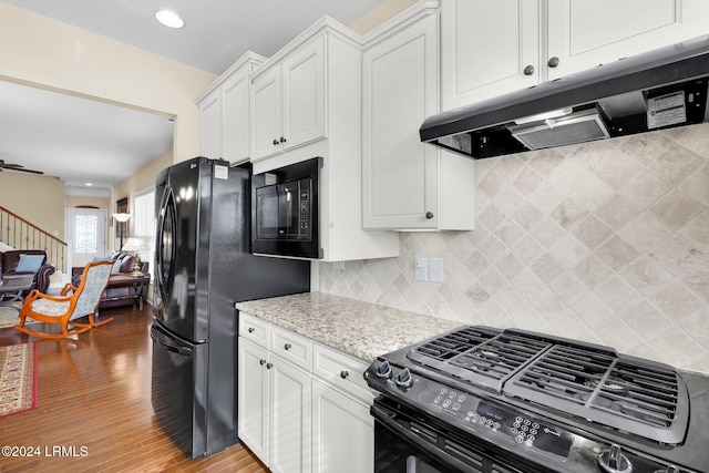 kitchen with white cabinetry, light stone counters, black appliances, light wood-type flooring, and backsplash