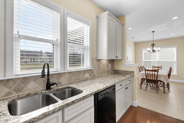 kitchen featuring sink, light stone counters, tasteful backsplash, hanging light fixtures, and black dishwasher