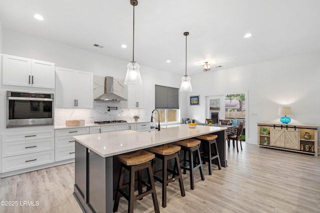 kitchen featuring light wood finished floors, a sink, wall chimney exhaust hood, backsplash, and appliances with stainless steel finishes