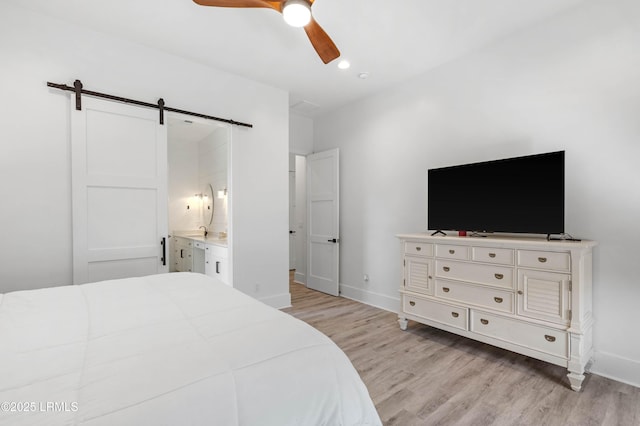 bedroom with a barn door, light wood-type flooring, a ceiling fan, and baseboards