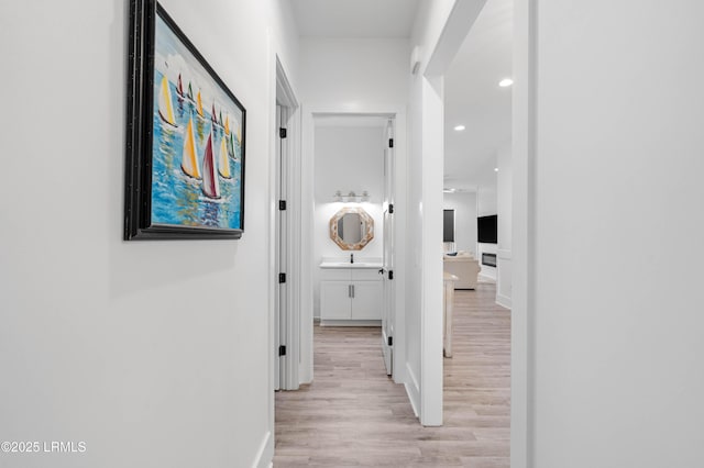 hallway featuring baseboards, recessed lighting, and light wood finished floors
