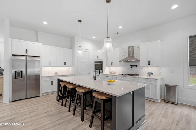 kitchen with light wood-type flooring, appliances with stainless steel finishes, wall chimney range hood, and decorative backsplash