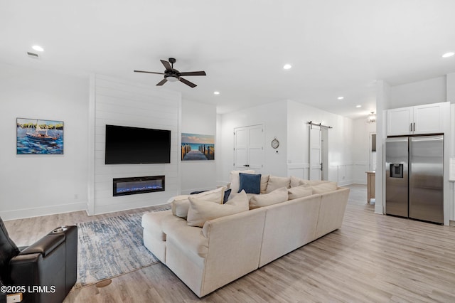 living room featuring light wood finished floors, recessed lighting, a barn door, a fireplace, and ceiling fan