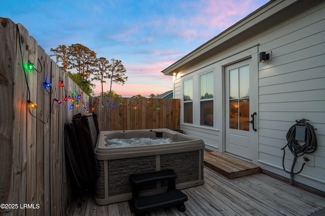 deck at dusk featuring fence and a hot tub