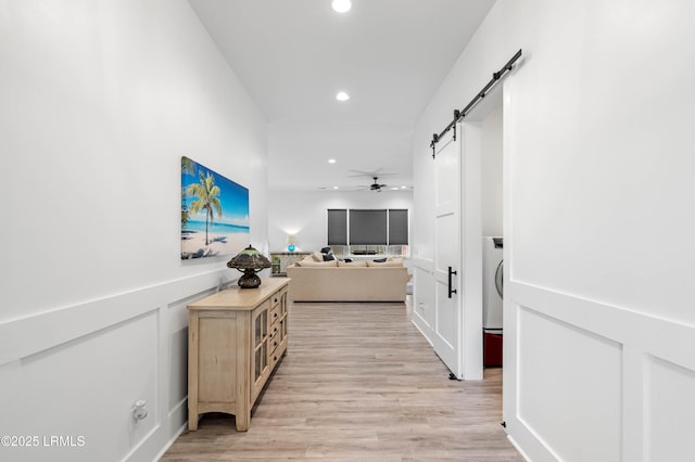 hall with a barn door, light wood-style floors, and recessed lighting