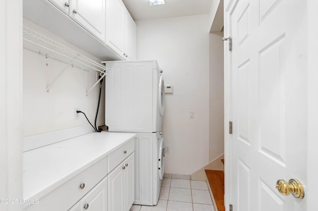 laundry area featuring stacked washer and clothes dryer, cabinet space, and light tile patterned floors