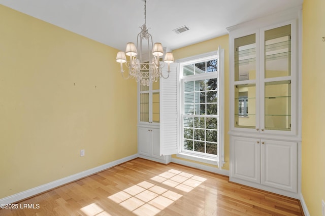 unfurnished dining area featuring light wood-style flooring, visible vents, baseboards, and a notable chandelier