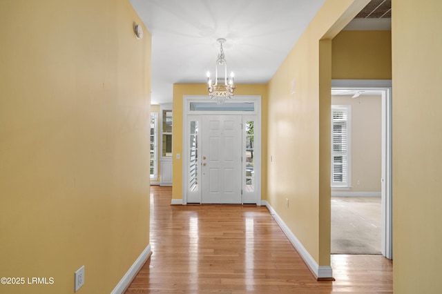 entrance foyer with light wood finished floors, baseboards, and an inviting chandelier