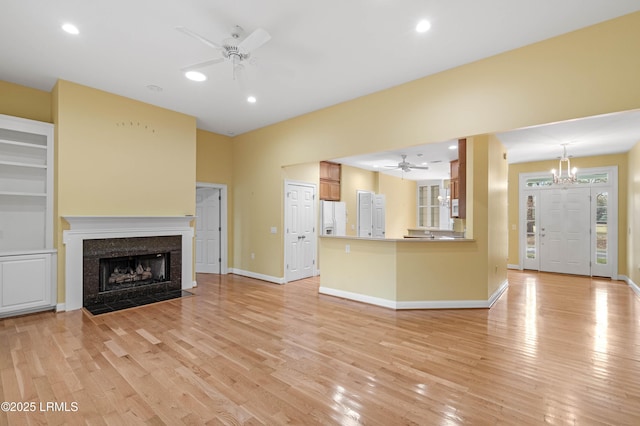 unfurnished living room with ceiling fan with notable chandelier, a high end fireplace, recessed lighting, and light wood-type flooring