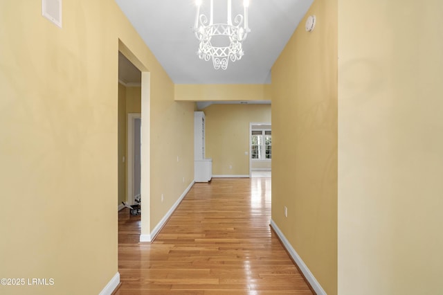 corridor with a notable chandelier, baseboards, light wood-style floors, and visible vents