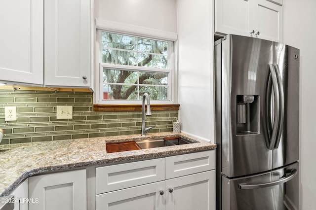 kitchen featuring stainless steel refrigerator with ice dispenser, sink, white cabinetry, light stone counters, and decorative backsplash