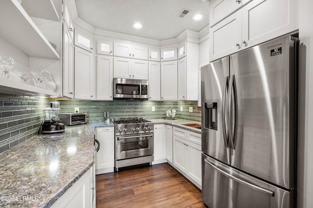 kitchen featuring appliances with stainless steel finishes, backsplash, white cabinets, dark hardwood / wood-style flooring, and light stone countertops