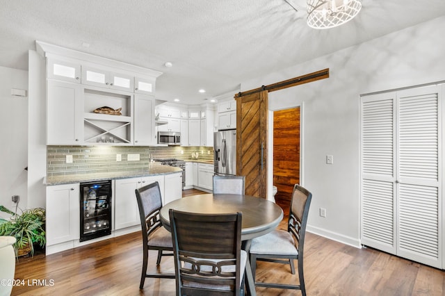 dining area with wine cooler, a barn door, dark wood-type flooring, and a textured ceiling