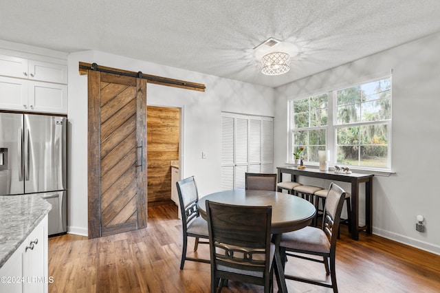 dining space with wood-type flooring, a barn door, and a textured ceiling