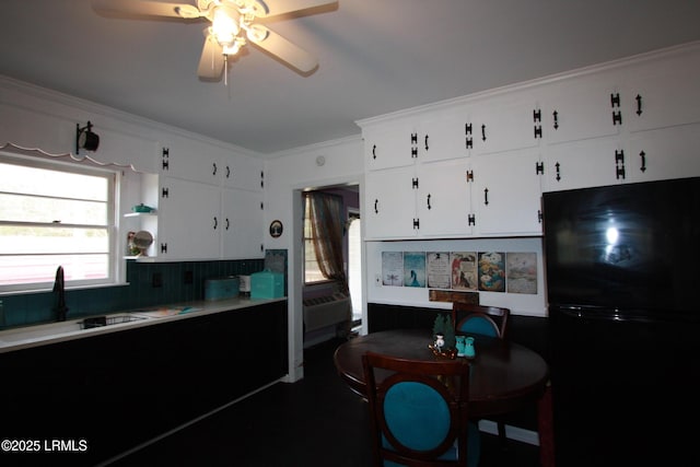 kitchen with white cabinetry, sink, ornamental molding, ceiling fan, and black fridge