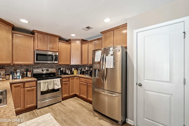 kitchen with light stone counters, backsplash, stainless steel appliances, and light hardwood / wood-style floors