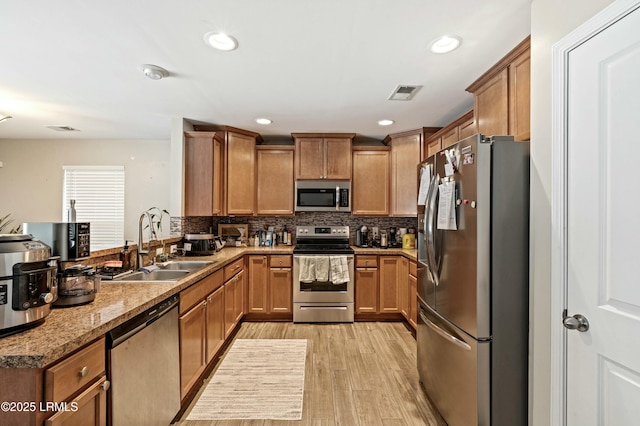 kitchen with appliances with stainless steel finishes, tasteful backsplash, sink, light stone countertops, and light hardwood / wood-style flooring