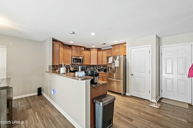 kitchen featuring tasteful backsplash, appliances with stainless steel finishes, kitchen peninsula, dark stone counters, and light hardwood / wood-style floors