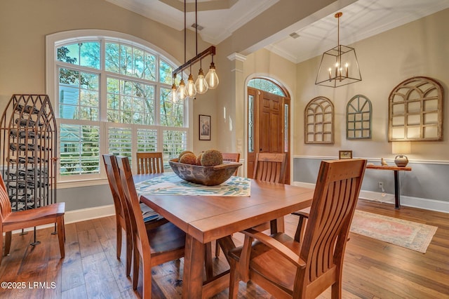 dining space with ornamental molding, hardwood / wood-style floors, a high ceiling, and a notable chandelier