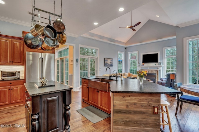 kitchen with high end refrigerator, sink, a center island with sink, and light wood-type flooring