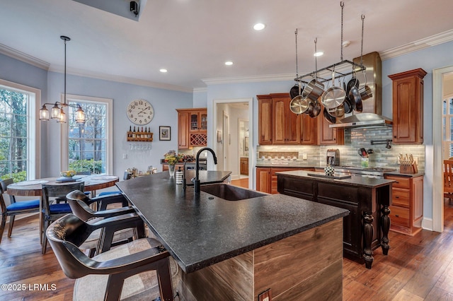 kitchen featuring wall chimney range hood, backsplash, sink, and a center island with sink