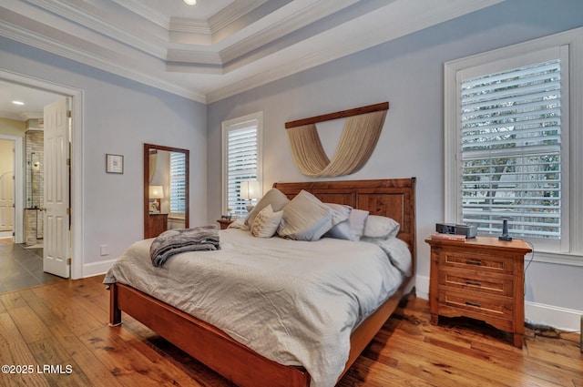 bedroom featuring hardwood / wood-style flooring, ornamental molding, a raised ceiling, and connected bathroom