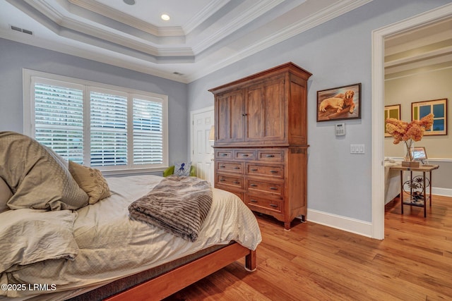 bedroom with ornamental molding, a tray ceiling, and light hardwood / wood-style flooring