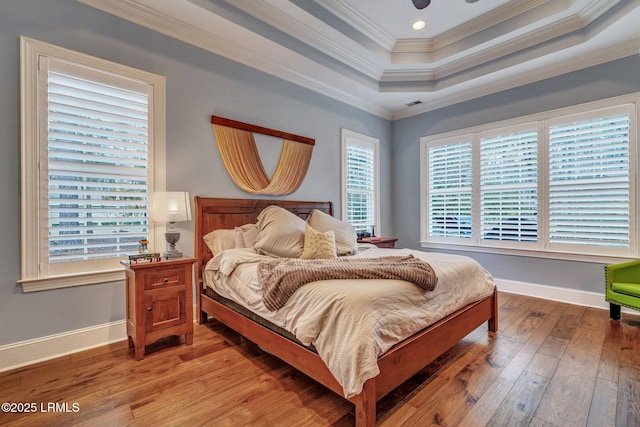 bedroom featuring wood-type flooring, ornamental molding, and a raised ceiling