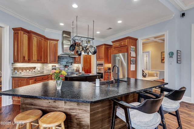 kitchen with wall chimney range hood, sink, high end fridge, dark hardwood / wood-style floors, and a large island with sink