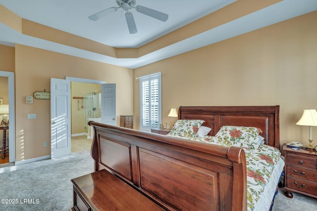 bedroom featuring light carpet, ensuite bath, a raised ceiling, and ceiling fan