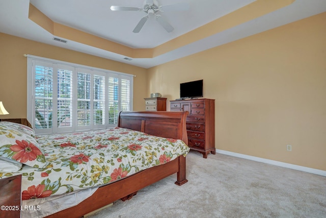 bedroom featuring light carpet, ceiling fan, and a tray ceiling