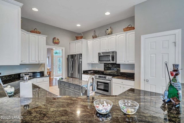 kitchen with dark stone countertops, kitchen peninsula, white cabinets, and appliances with stainless steel finishes