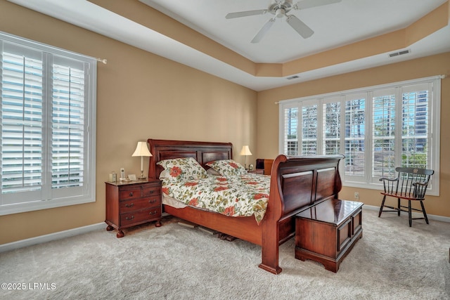 carpeted bedroom featuring multiple windows, a raised ceiling, and ceiling fan