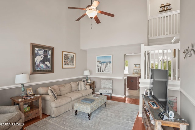 living room featuring ceiling fan with notable chandelier, a towering ceiling, baseboards, and wood finished floors