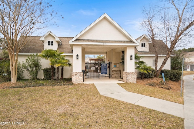 view of front facade with brick siding, roof with shingles, stucco siding, a front yard, and a gate